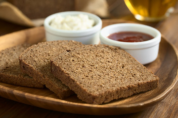 Pumpernickel Brotscheiben auf Holzteller, fotografiert mit natürlichem Licht (Selektiver Fokus, Fokus diagonal durch die Brotscheibe)