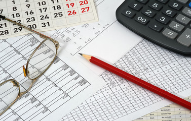 Papers with figures, calendar, glasses, red pencil and calculato