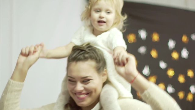 Young mother is playing with her little daugther. Little cute baby girl sits on her mother's shoulders
