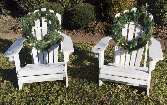 White Adirondack chairs decorated with Christmas holiday wreaths on front lawn. Horizontal.