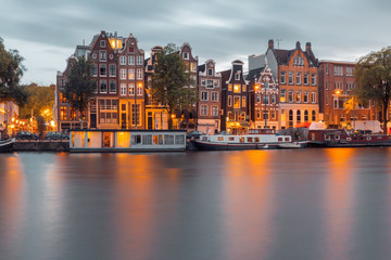 Fototapeta na wymiar Amsterdam canal Amstel with typical dutch houses and boats during twilight blue hour, Holland, Netherlands.