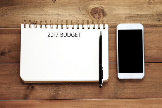 2017 budget word on blank notebook paper, pen and smart phone on