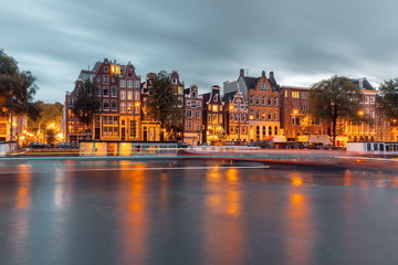 Fototapeta na wymiar Amsterdam canal Amstel with typical dutch houses, houseboat and luminous track from the boat during twilight blue hour, Holland, Netherlands.