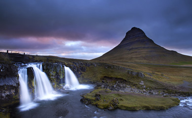cloudy sunset the top of Kirkjufellsfoss waterfall with Kirkjufell mountain in the background on the north coast of Iceland's Snaefellsnes peninsula taken white a long shutter speed.