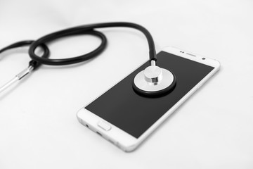 Medical stethoscope tool over the surface of a mobile smart phone, composition isolated over the white background