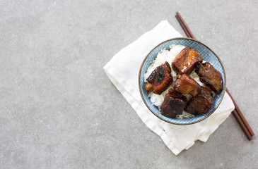 Chinese sweet and sour ribs in a blue bowl on a white napkin. Dark gray stone background. Copy space. 