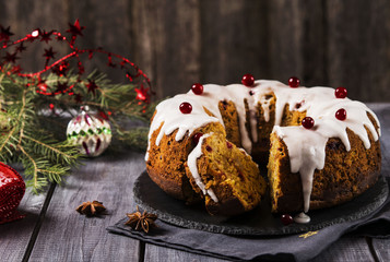 Christmas homemade cake with nuts, apples and cranberries with icing on dark wooden background. Selective focus 