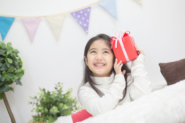 Happy Asian girl shaking a present to guess whats inside