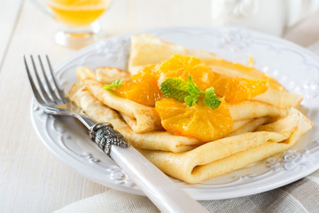 Thin crepes with orange citrus sauce for breakfast on light background. Selective focus.