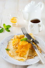Thin crepes with orange citrus sauce for breakfast on light background. Selective focus.