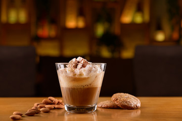 Cocktail with alcohol, coffee, cream and cinnamon powder . Cookies and almonds on a wooden table.