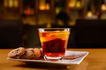 Cocktail with alcohol, tea, lemon slices and raisins. Cookies and cinnamon powder in a white plate.