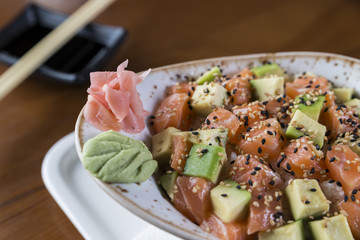 Sushi plate with fresh salmon and avocado cubes. Chopsticks and soy sauce at the background. 
