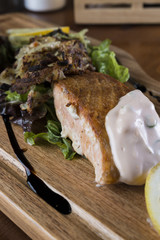Salmon filet with baked onion, green salad, limes and fresh sauce on a wooden platter.