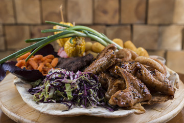 Wooden platter with meat, potatoes,carrots, corn, cabbage and onion rings.