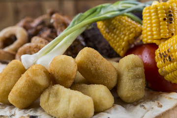 Wooden platter with meat, potatoes,carrots, corn, cabbage and onion rings.