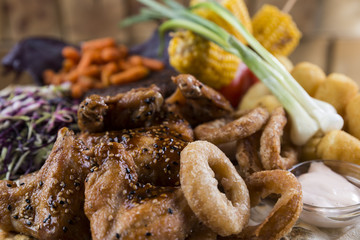 Wooden platter with meat, potatoes,carrots, corn, cabbage and onion rings.