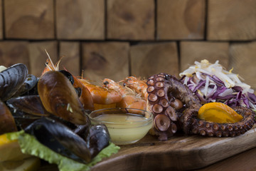 Seafood set with octopus, shrimps and shells on a wooden platter.