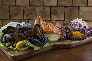 Seafood set with octopus, shrimps and shells on a wooden platter.
