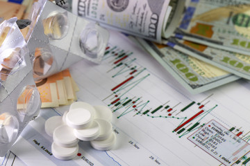 Currency exchange trading worries .Hundred us dollar bills and fifty euro bills in background. Currency us euro exchange chart under the bills.  Piles of sedative medical pills, empty pills packs.