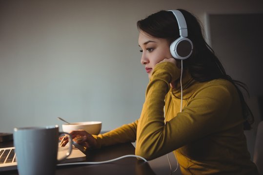 Woman listening to headphones while using laptop