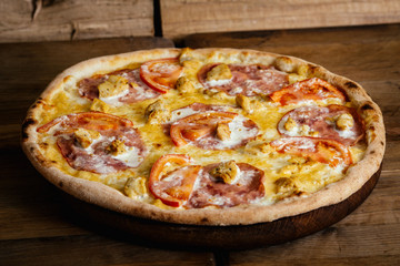 Whole pizza with chicken, ham and tomatoes on wood table with ingredients
