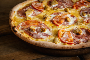 Whole pizza with chicken, ham and tomatoes on wood table with ingredients