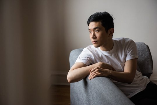 Thoughtful Man Looking Through Window While Sitting On Sofa At Home