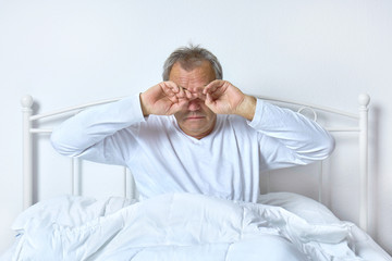 Senior im Bett im Schlafzimmer beim Aufwachen