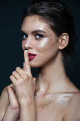 Happy woman with sparkles on her face showing silence sign