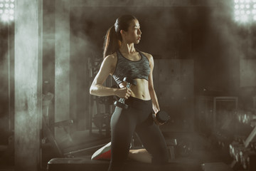 Plakat Toned picture,Asian fitness girl lifting a dumbbell at fitness center.