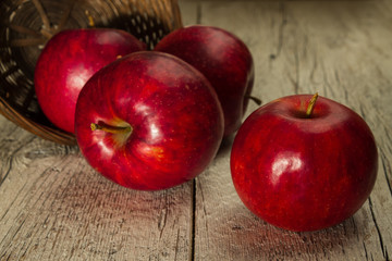 red apples in a wicker basket scattered on a wooden background