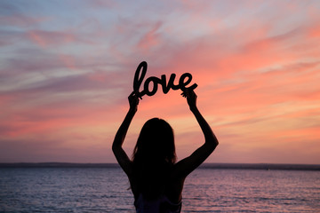 Female silhouette on sunset background with the word love in han