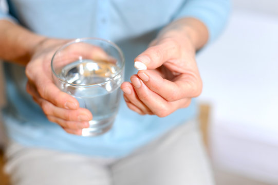 Frau hält eine Tablette und ein Glas Wasser in der Hand