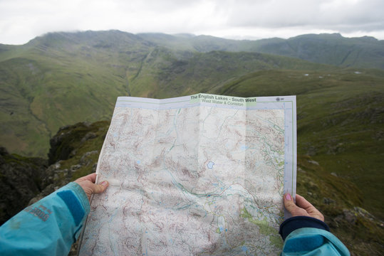 A woman checks her map while looking towards Great Langdale valley from the Langdale Pikes, Lake District, Cumbria