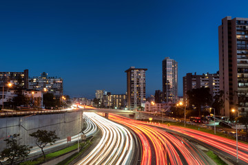 Fototapeta premium Light trails over H1 highway in downtown Honolulu, Hawaii during sunset golden hour