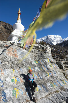 A woman trekking in the Langtang valley stops near a colorful Mani Stone wall below a Stupa decorated with Buddhist prayer flags, Langtang Region, Himalayas, Nepal