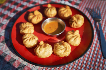 Plate of traditional fried Nepalese momos on the red plate with sauce in soft-focus