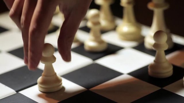 Panning shot of a chess board with a hand moving the white pawn.