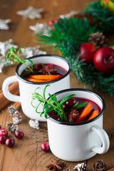 Christmas Hot mulled wine in white rustic mugs with orange slices, cranberry, anise and cinnamon sticks on wooden background, selective focus. Winter Holiday time concept