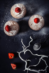 Obraz na płótnie Canvas Christmas cupcakes with strawberries and powdered sugar on black background. Top view. Festive winter food backdrop.