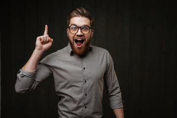 Excited happy bearded man in eyeglasses pointing finger up