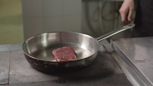 Closeup of male hands placing meat fillet on hot frying pan and adding herbs
