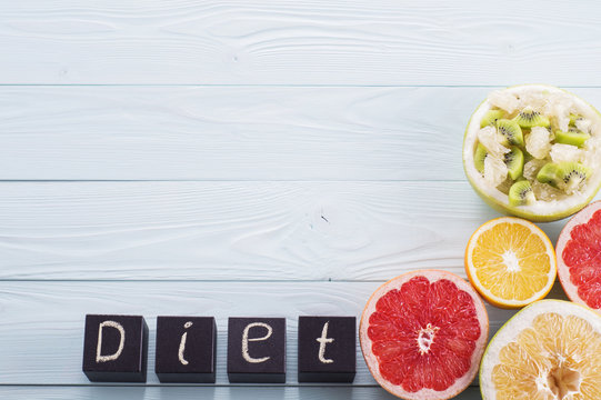 Diet word made with building black wooden blocks with fruit salad and the halves of citrus, grapefruit, orange, sweetie on a blue wooden background with copy space. Diet concept, top view.