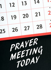 The words Prayer Meeting Today in white text on a blackboard underneath a wall calendar as a reminder