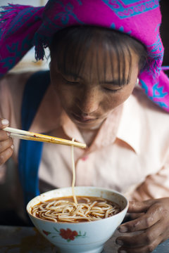 A Miao woman eats a bowl of noodles in Yunnan Province, China