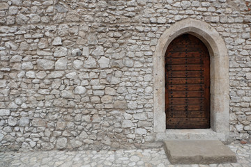Heavy closed wooden door with pointed arch in the white cobble stone wall of a medieval fortress, made of riveted wood planks