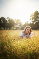 Beautiful blonde, girl, woman, lying in a field in backlight, seaming light and smiling