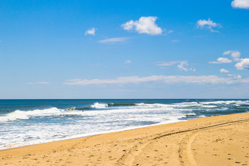 Ocean beach with footprints on sand on background of blue sky