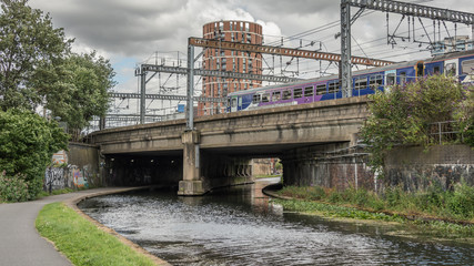 Train crossing a bridge  over a canal in a urban city transport photograph. Power cable and city scape.